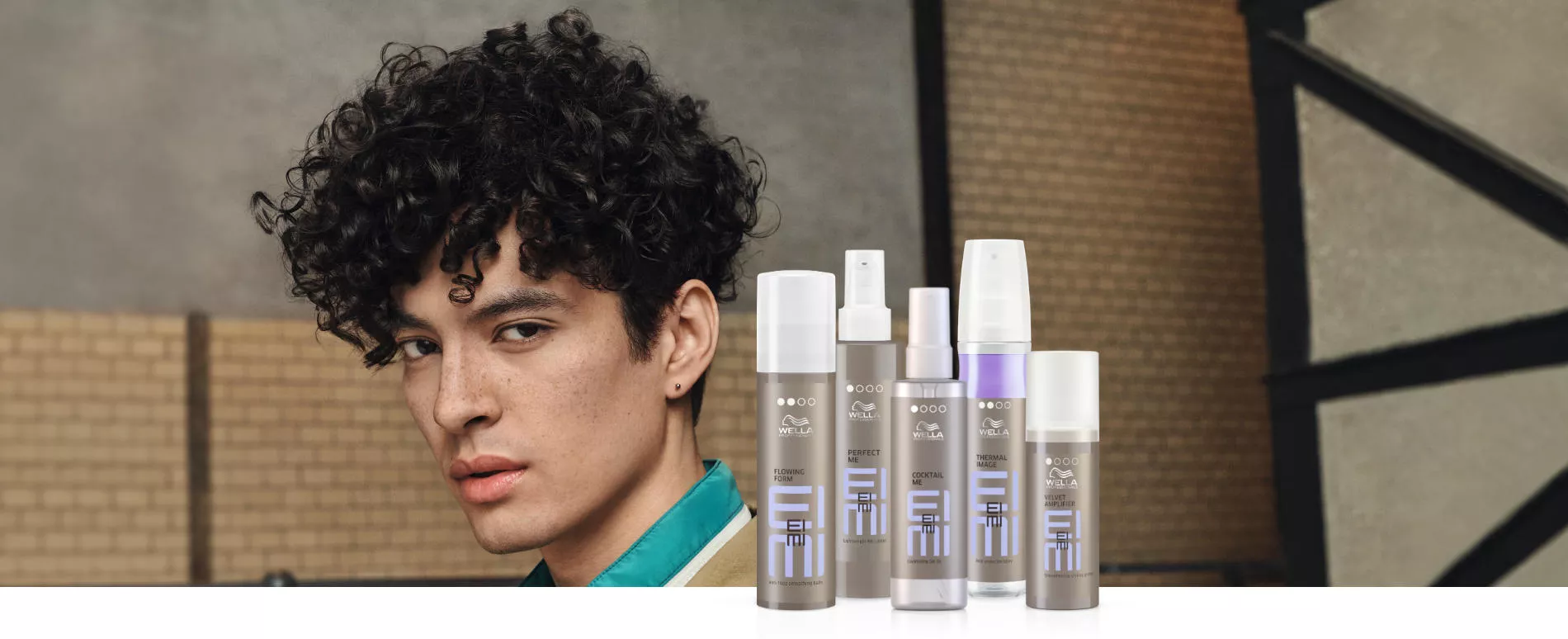 Headshot of a male model with forehead-length very thick, tightly curled black hair, plus 5 bottles of EIMI styling product