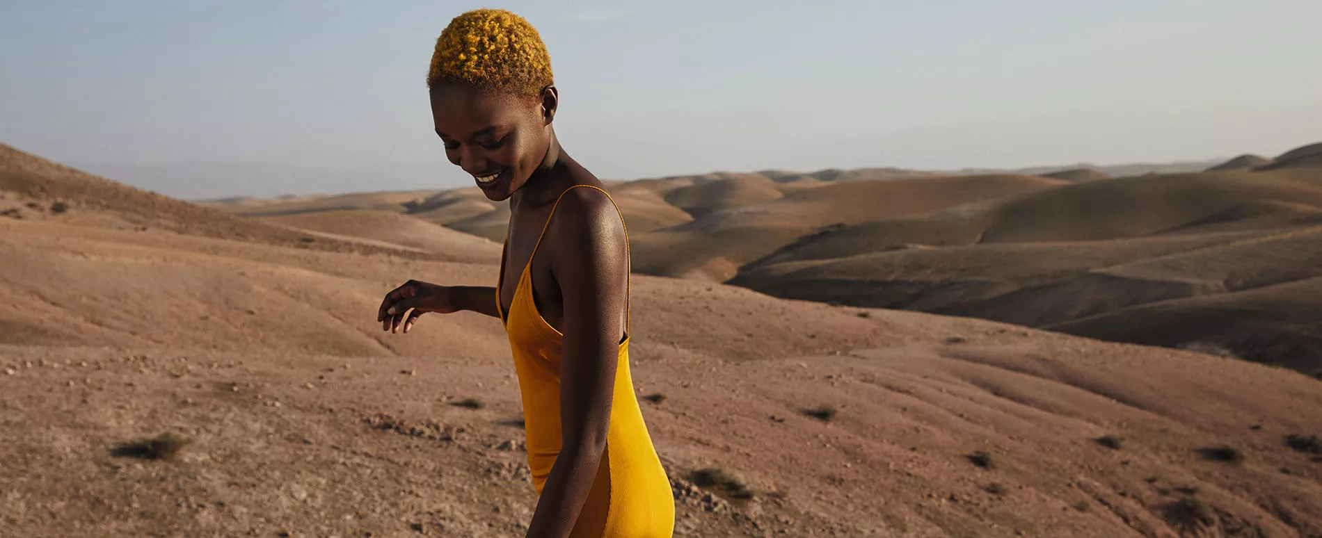 Model with golden yellow afro hair, wearing a golden dress with a panoramic view in the background