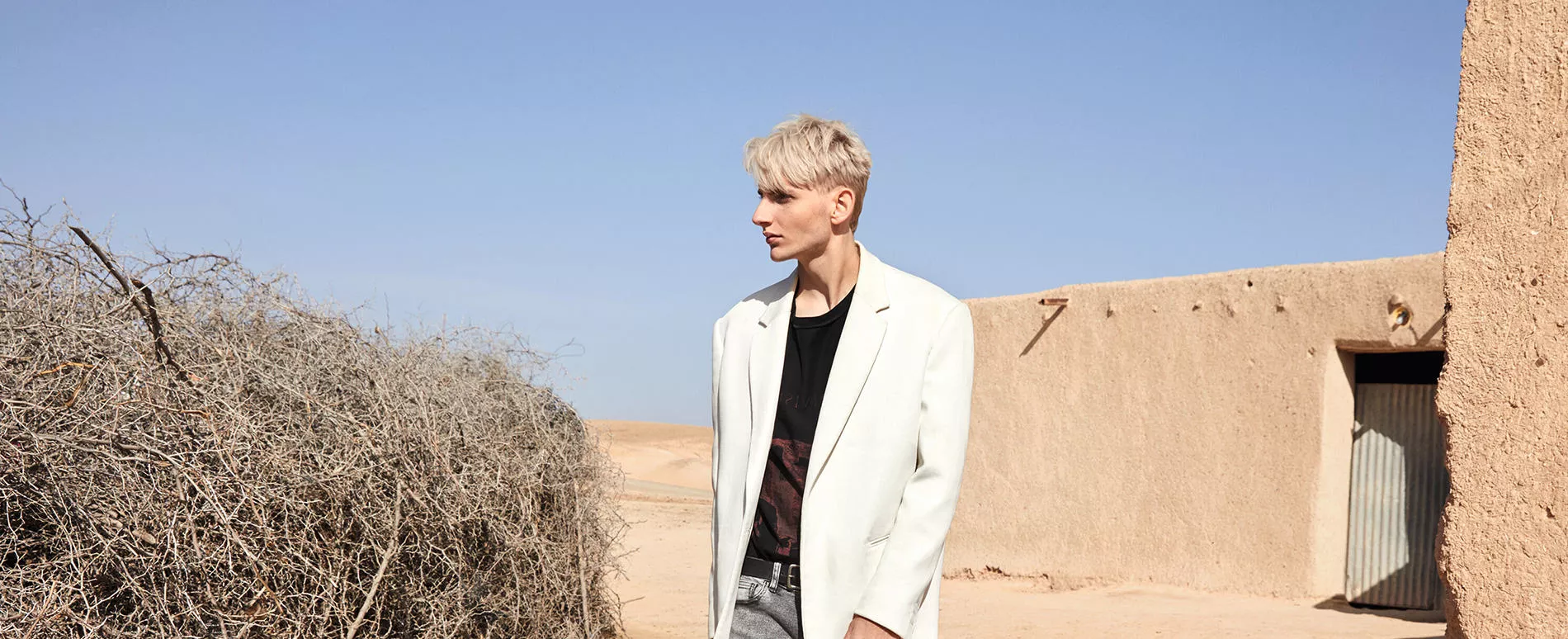 Male model with layered blonde hair  wearing a white blazer and a black top