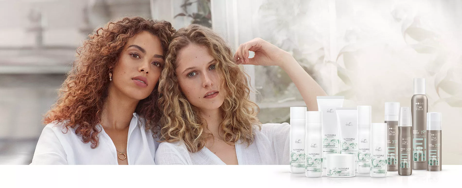 Zwei Frauen mit schulterlangen Korkenzieherlocken in weißer Kleidung sitzen beisammen, plus NUTRICURLS Produktflaschen