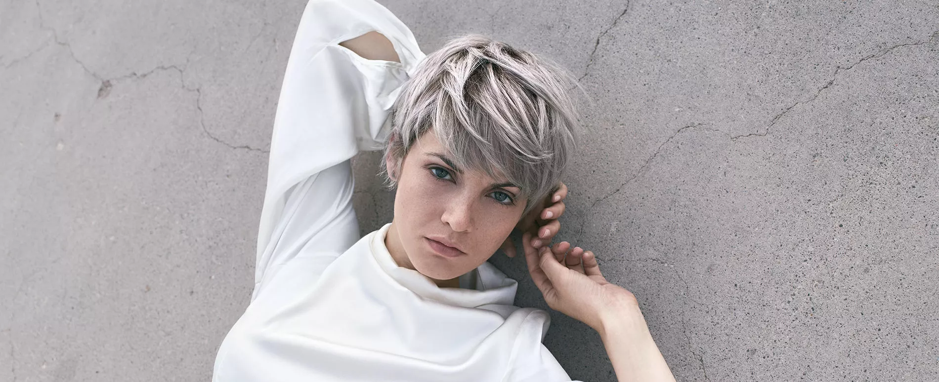 Mujer con un corte de pelo estilo pixie de color gris suave tumbada en un suelo color pizarra