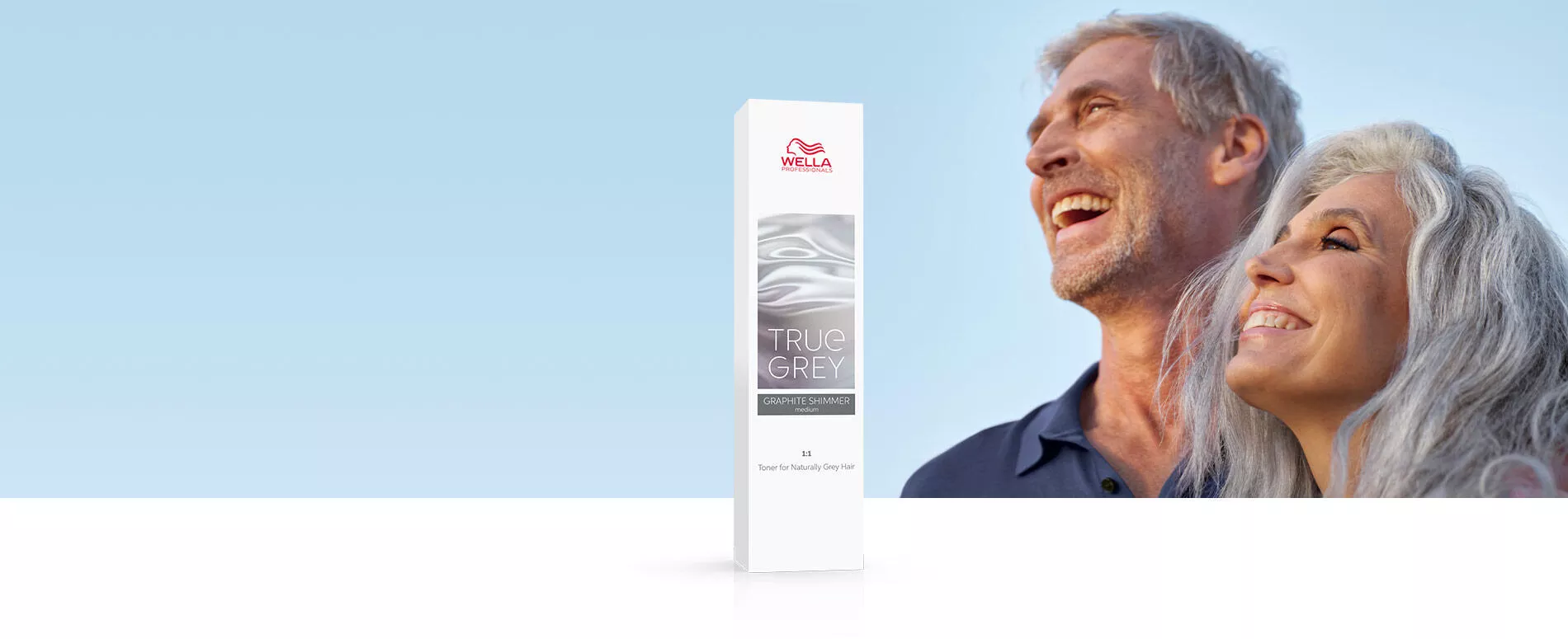 Un hombre y una mujer con cabello gris natural riéndose frente al sol con una botella de matizador True Grey