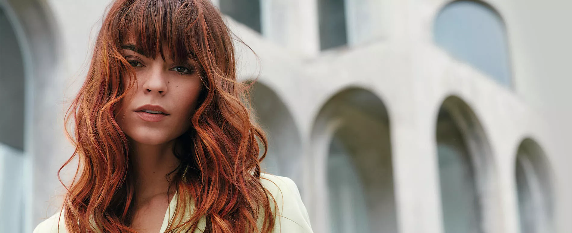 A woman with red curled hair and fringe,  achieved with Wella Professionals Koleston Perfect Lights