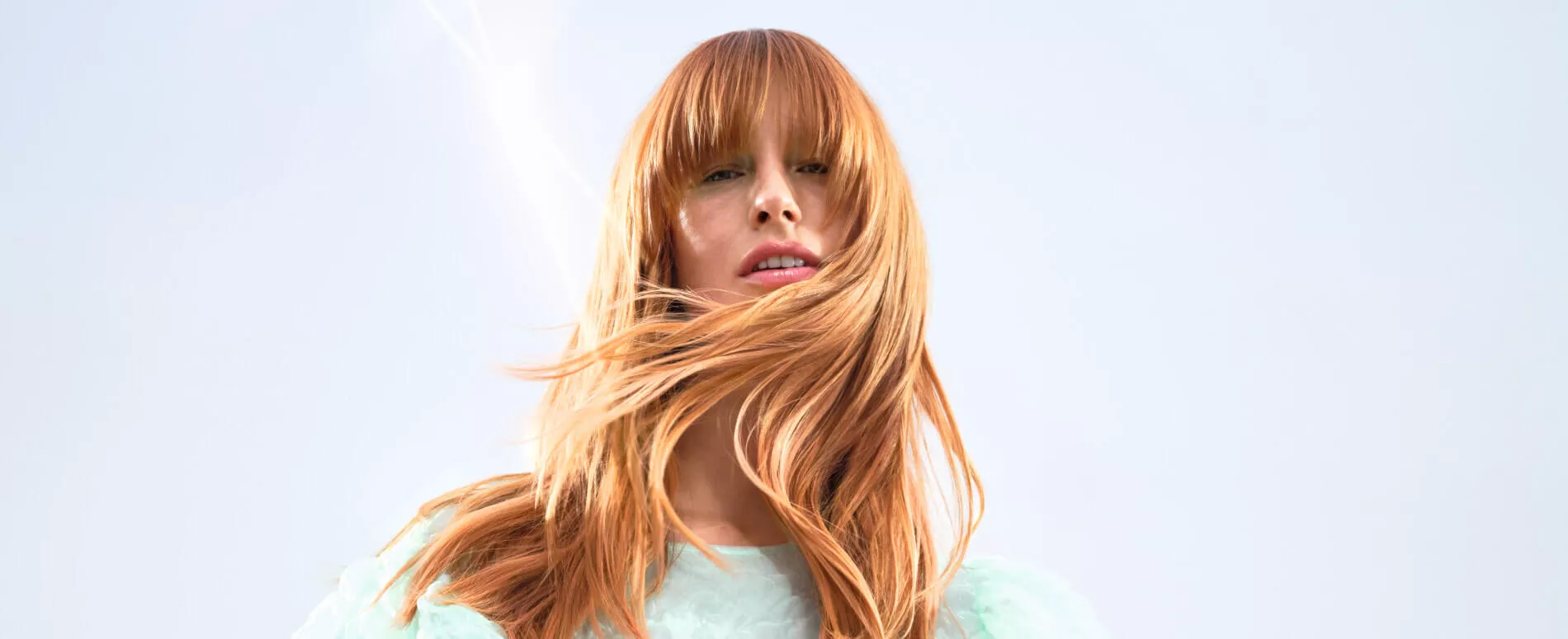 Ein Model mit kupferfarbenem Haar schaut in die Kamera und ihre Haare werden vom Wind verweht
