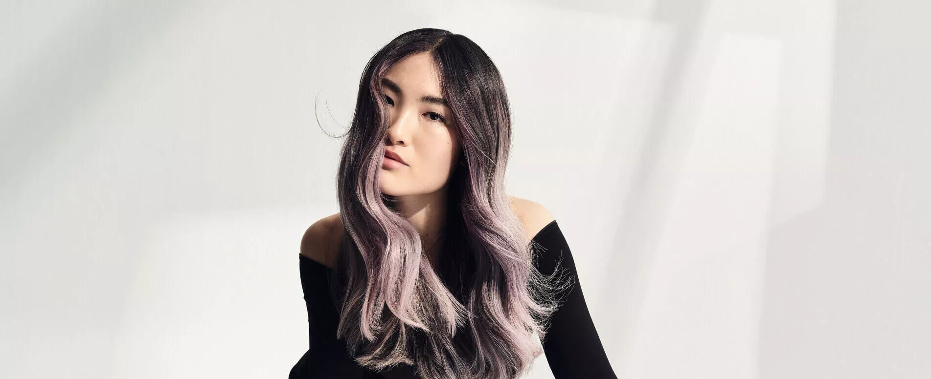 Model with dark lavender hair is dressed in black and leaning to one side