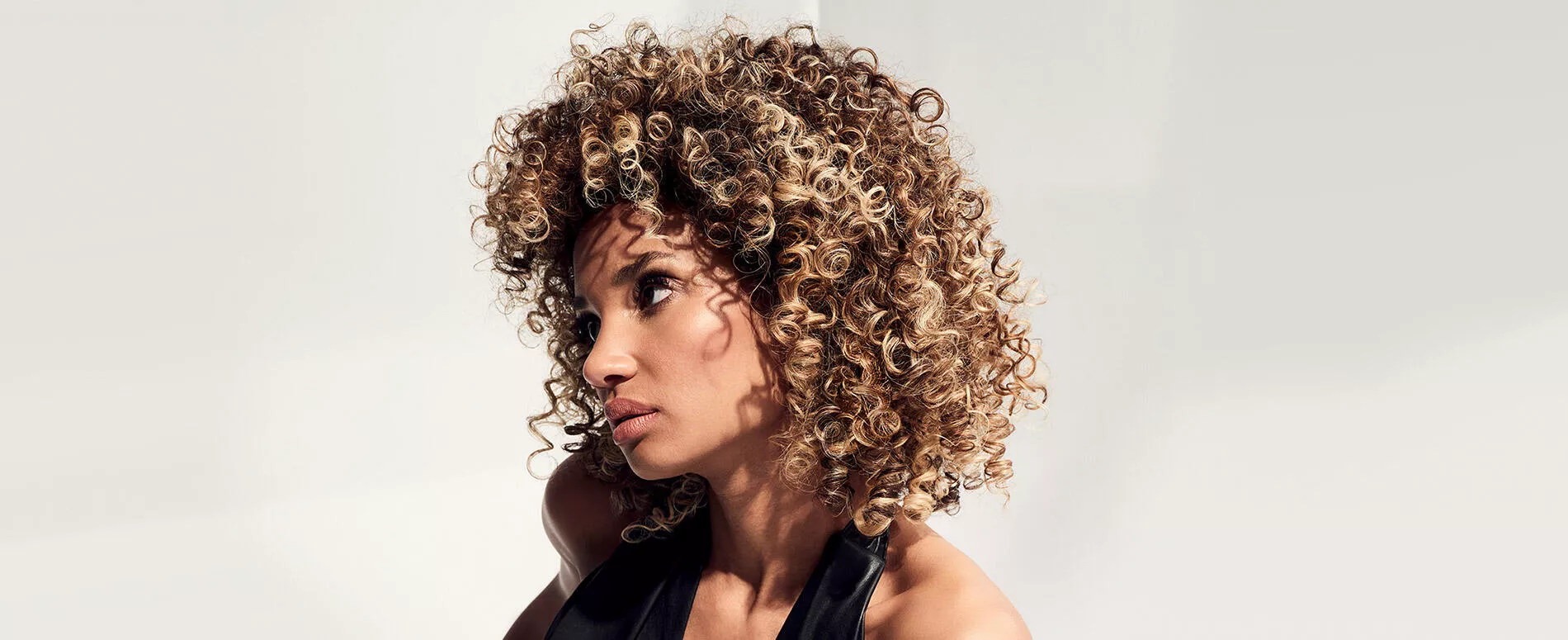 Model with curly, highlighted hair looks to the side