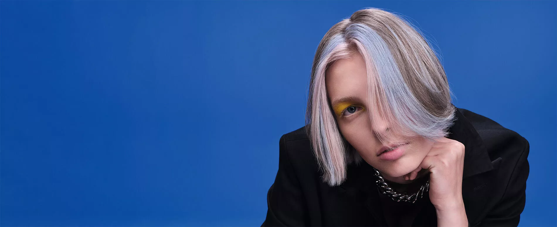 Blonde model wit light blue locks, with blocked face frame color service, in front of a blue background