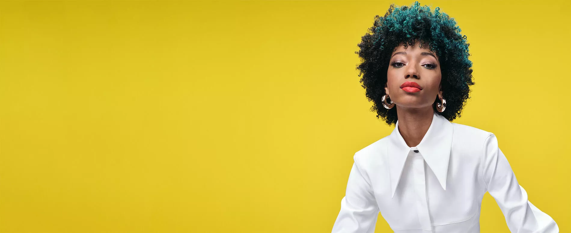 Model with with brunette and green afro hair with contrast blocking colour service, on a yellow background