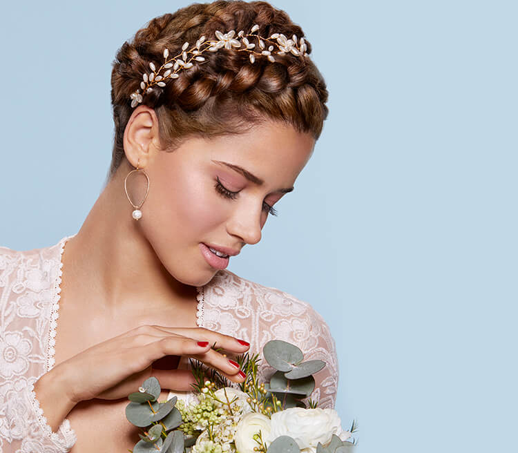 Side-facing image of model wearing bridal braids wedding hairstyle and carrying a bouquet of flowers. 